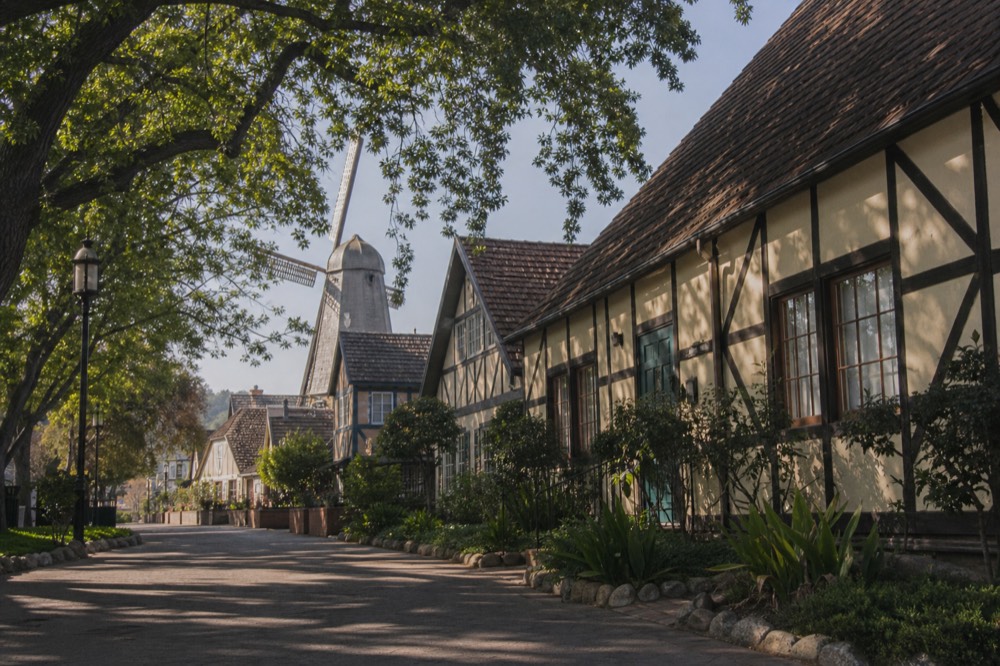 A quiet Danish-style street in Solvang with half-timbered buildings and a wooden windmill under soft morning light, no text, no logos, no people